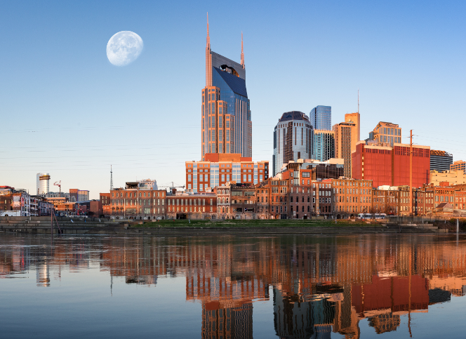 Nashville cityscape at night with the iconic AT&T Building, moon, and skyline reflection in the river.