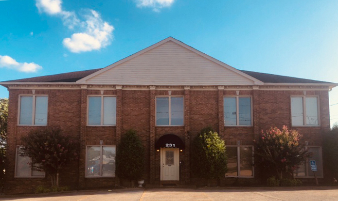 Two-story brick building with large windows and bushes at the entrance, number "231" displayed